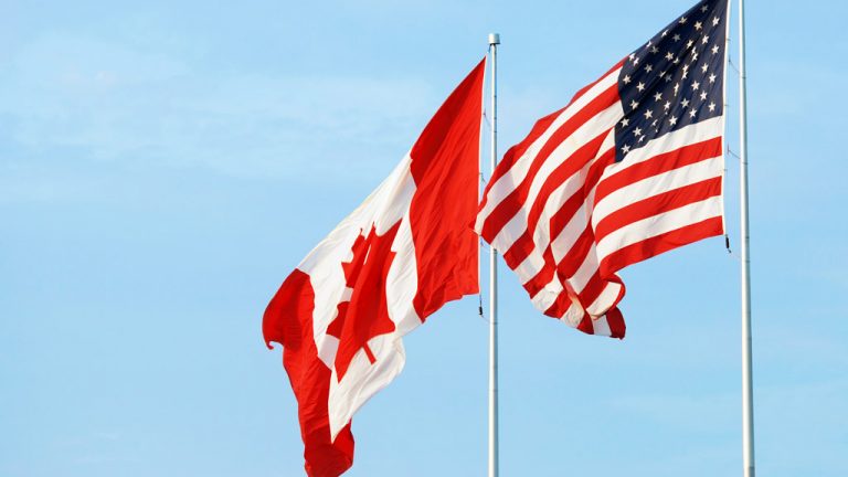 A photo of the Canadian and American flags flying on flagpoles next to each other.