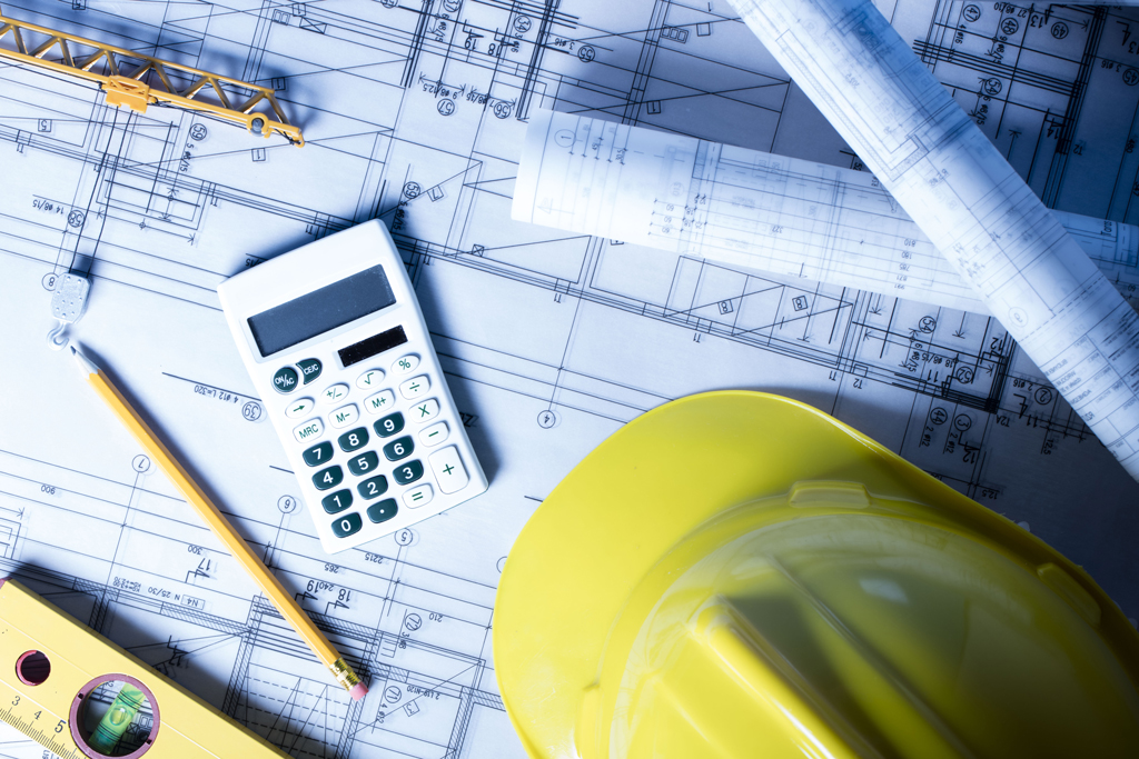 A pencil, calculator, level and hardhat rest on top of the blueprints for a building.