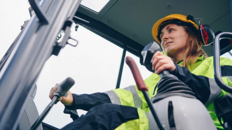 A woman in safety equipment operating a heavy equipment machine.
