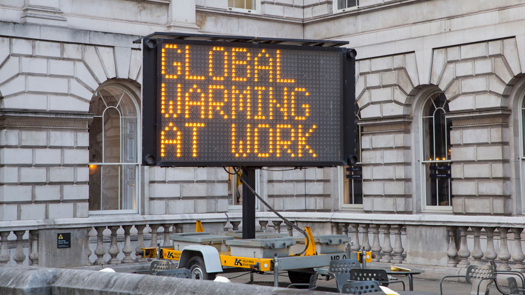 An electronic construction sign in front a building that says "Global Warming At Work."