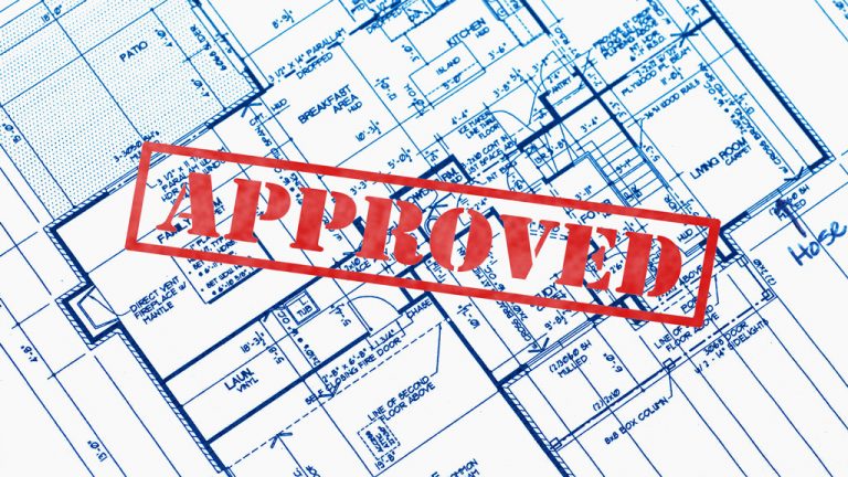 A photo of blueprints for a building with the word "approved" stamped in red on it.