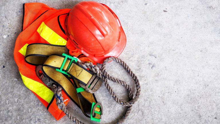 A red hardhat, a harness, a safety vest and a rope laying on the ground