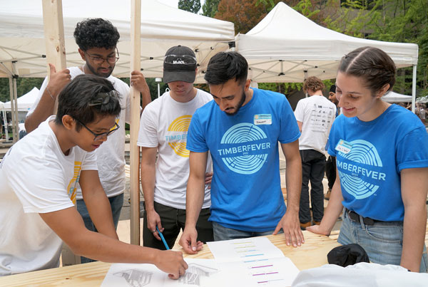 Paulo Temporada, engineering student at McMaster University, reviews drawings for a TimberFever project with his team including Dinura Fernando and Todd Collis, both Toronto Metropolitan University students. Advice comes from Ishareet Merwaha and Alexandra Winslow of the organizing committee for TimberFever 2022.
