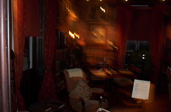 Two images shot by the photographer, one before and one after midnight.  In the first photo orbs of light, believed by some to indicate a supernatural presence, surround an antique umbrella stand at Eldon House.  In the second, a library chair and a museum display card in the foreground are in full focus, while the background appears wildly out of focus.