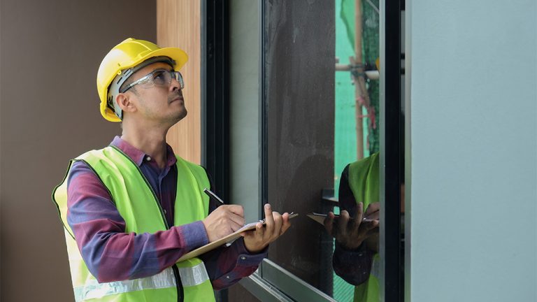 A construction worker takes notes on a clipboard while examining a window.