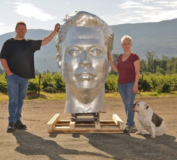 Kevin Stone, his wife Michelle and dog Harley stand in front of his commissioned statue of Elon Musk. The giant head was made to be mounted on the body of a goat. Stone and his wife invite local schools and students to tours and workshops at their Chilliwack, B.C. garage to inspire the youth to get into the skilled trades.