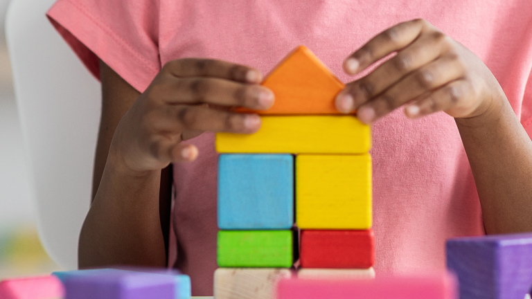 a child in a pink shirt stacking blocks into the shape of a house.