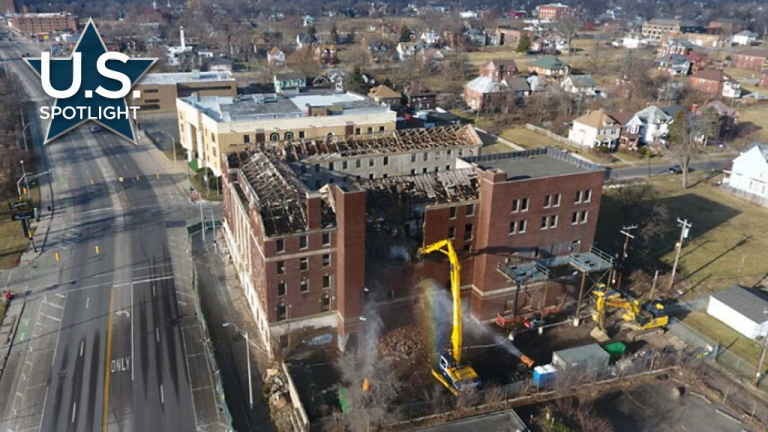 A high reach excavator attacks the former YMCA on Detroit's east side. Downtown Detroit can be seen in the distance.