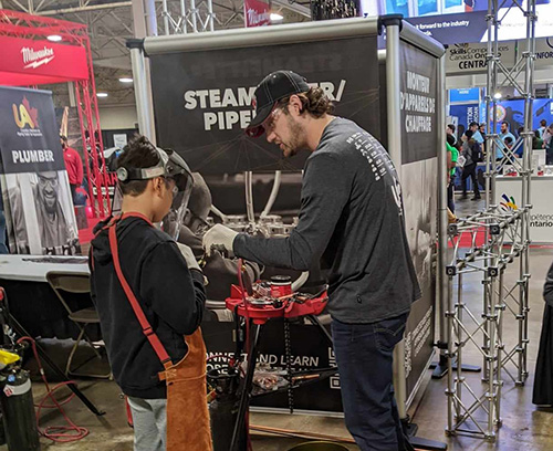 A student receives a hands-on lesson at a UA steamfitter/pipefitter booth May 6.