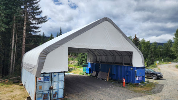 Stabl Shelters arched fabric cover shown with open front and back and resting on shipping containers.