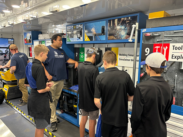 A staff member from Skills Ontario instructs a group of boys using a welding simulator on the Trades & Tech Truck at the Level Up! Career Fair in Kitchener.