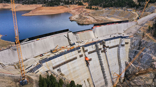 The $565 million project is hiking the height of the dam by building 118 concrete steps from the bottom of the existing structure to the new dam crest. Each step is four feet tall with a two-foot-long setback from the step below. Roller Compacted Concrete is being used to raise the dam.